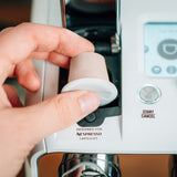 Hand inserting a 100% home compostable, Nespresso® compatible coffee capsule into an espresso machine.
